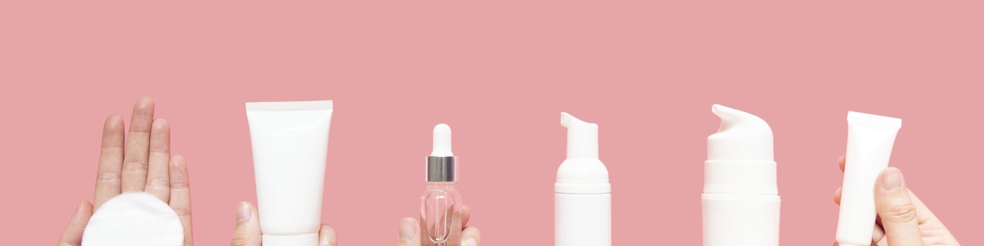 Skincare routine step for healthy skin - Woman hands holding facial cotton pad, foam, essential oil, serum, lotion and eye cream packaging on pink background. Beauty and cosmetic concept.